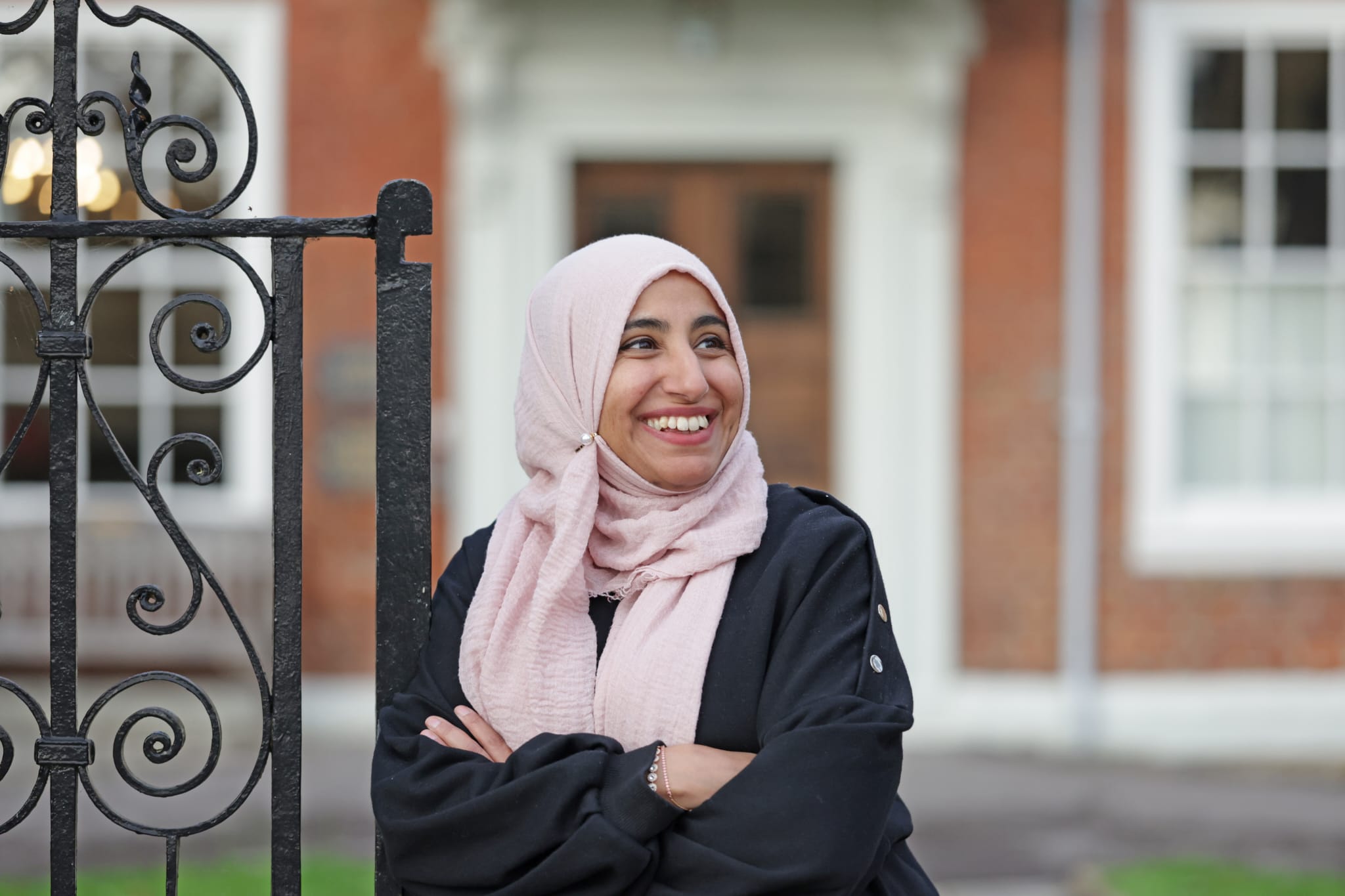 Dr Abida Malik smiling beside a wrought-iron gate