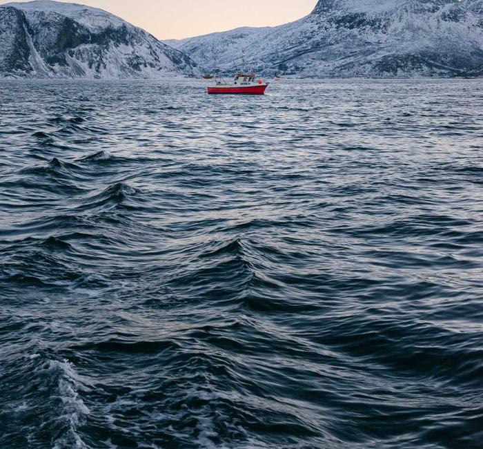 A small red boat on open water below snowy mountains